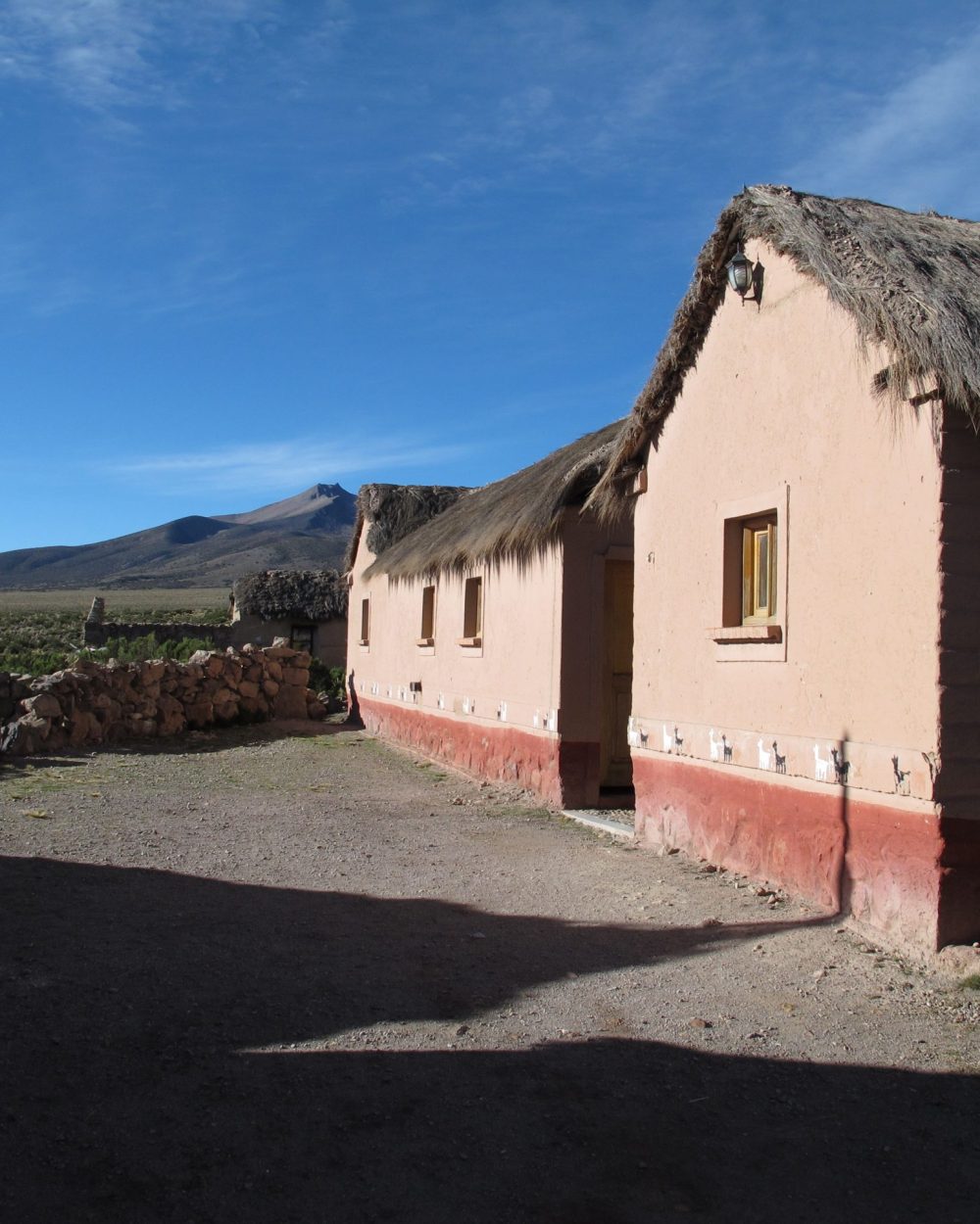 Bâtiment en adobe de Tomarapi aux toits de chaume devant le Nevado Sajama
